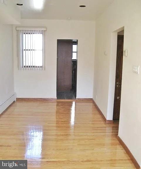 spare room with baseboard heating, light wood-type flooring, and baseboards