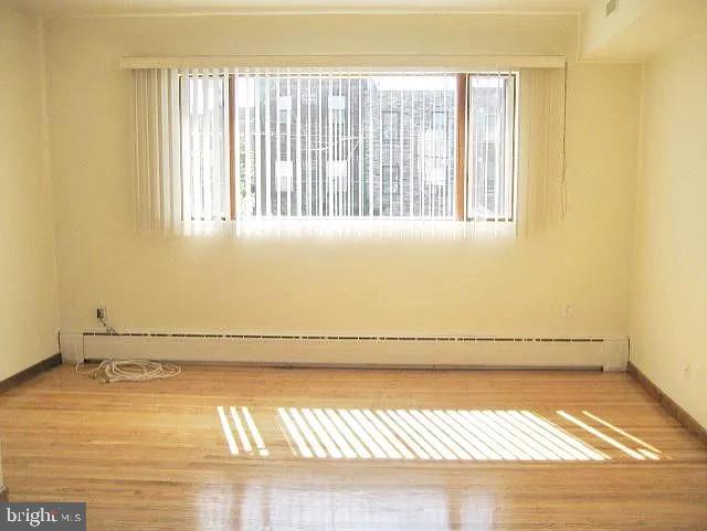 empty room featuring baseboard heating, wood finished floors, and baseboards