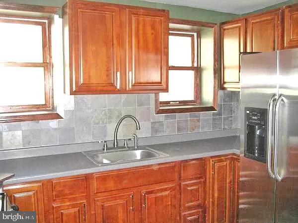 kitchen featuring brown cabinets, stainless steel fridge, decorative backsplash, and a sink