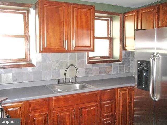 kitchen with stainless steel fridge, decorative backsplash, brown cabinets, light countertops, and a sink