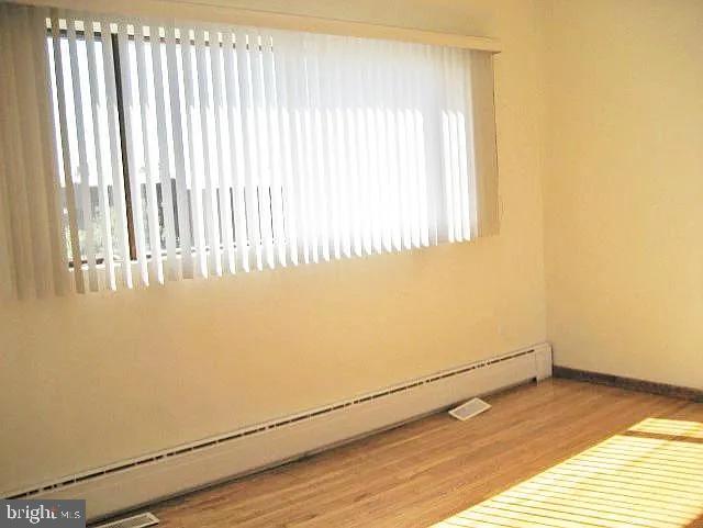 unfurnished room featuring a baseboard heating unit, wood finished floors, and baseboards