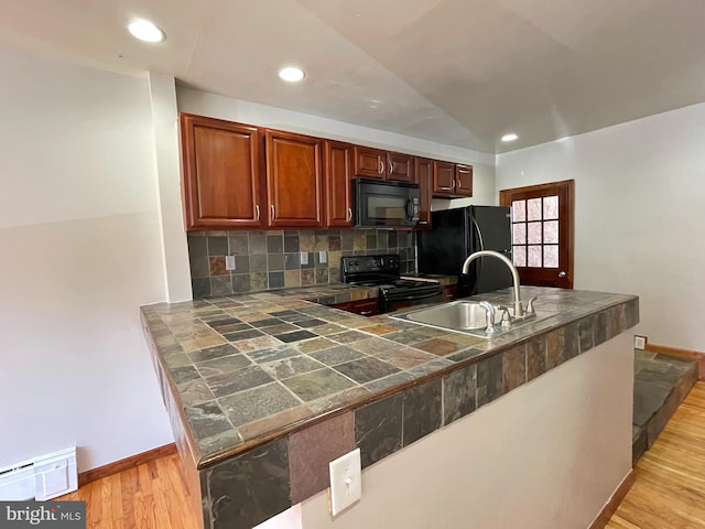 kitchen with a baseboard radiator, a sink, light wood-type flooring, decorative backsplash, and black appliances