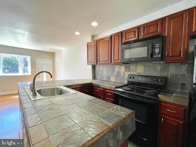 kitchen featuring a peninsula, a sink, tile counters, black appliances, and tasteful backsplash