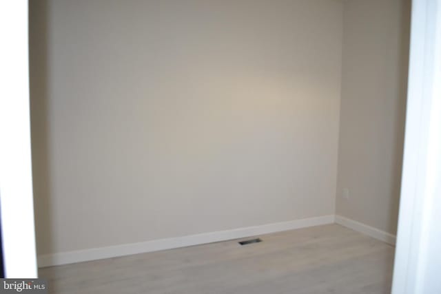 empty room with light wood-type flooring, visible vents, and baseboards