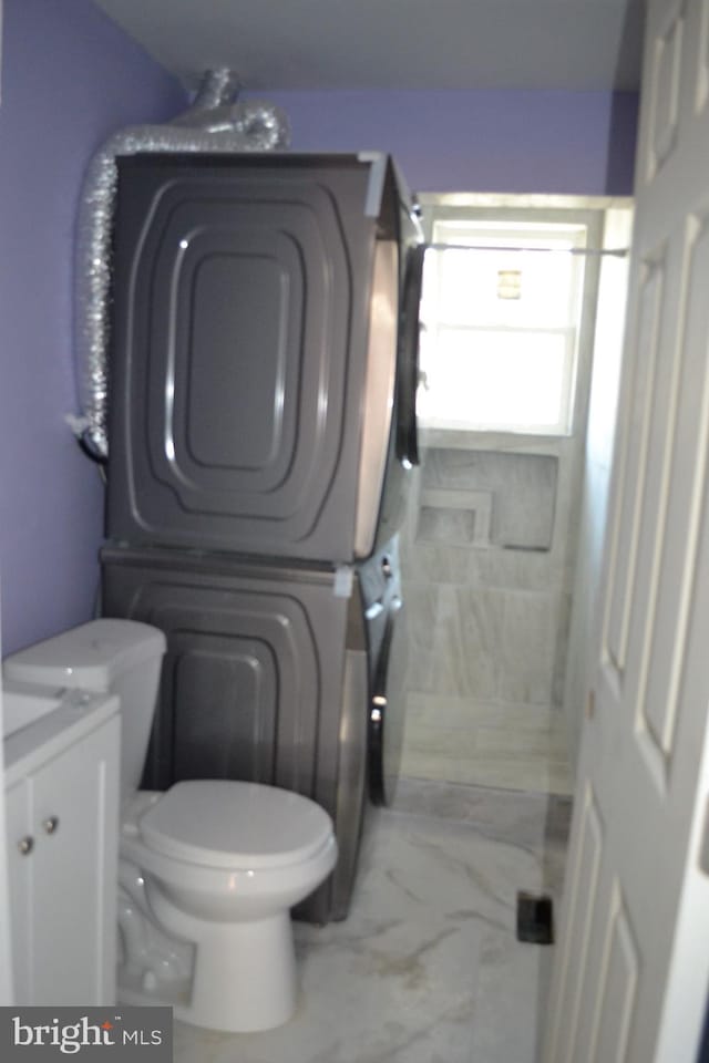 bathroom featuring marble finish floor, toilet, and stacked washing maching and dryer