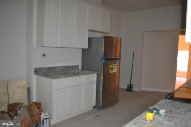 kitchen featuring light stone countertops, white cabinets, light wood-style floors, and freestanding refrigerator