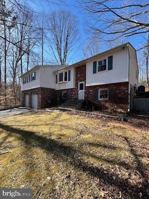 bi-level home featuring a garage, entry steps, concrete driveway, and brick siding