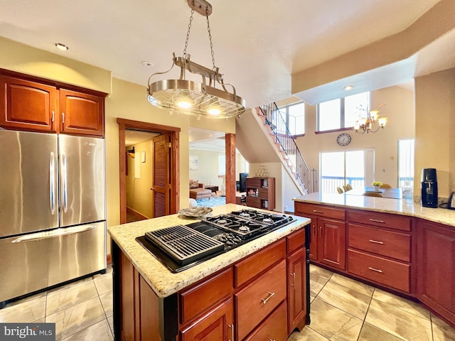 kitchen with a chandelier, black gas stovetop, light stone countertops, freestanding refrigerator, and a center island