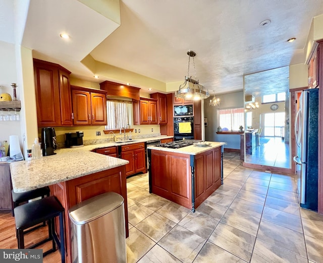 kitchen featuring black appliances, light stone counters, a peninsula, and a sink