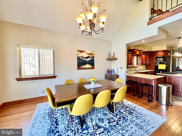 dining room with a chandelier, high vaulted ceiling, light wood-style flooring, and baseboards