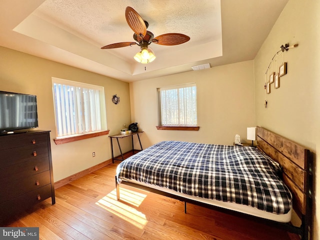 bedroom featuring light wood-style floors, a raised ceiling, visible vents, and a textured ceiling