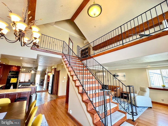 staircase featuring wood finished floors, baseboards, a high ceiling, and an inviting chandelier