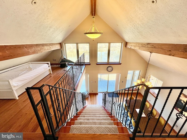 staircase with plenty of natural light, lofted ceiling with beams, and wood finished floors