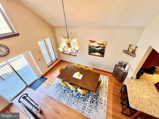 dining room featuring baseboards, high vaulted ceiling, wood finished floors, and a notable chandelier