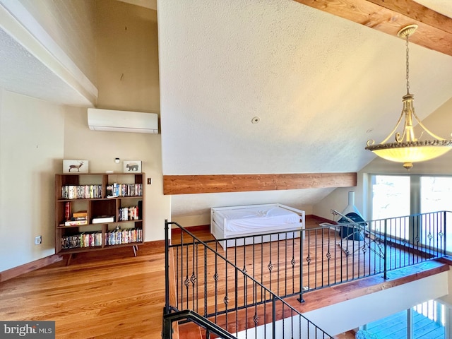 interior space with lofted ceiling, wood finished floors, an upstairs landing, baseboards, and a wall mounted air conditioner