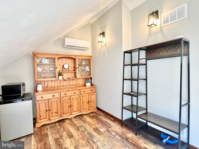 bar with visible vents, a wall unit AC, wood finished floors, refrigerator, and vaulted ceiling