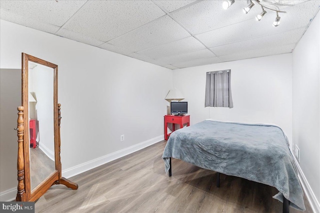 bedroom featuring a drop ceiling, wood finished floors, and baseboards