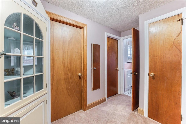 hall with light carpet, a textured ceiling, and baseboards