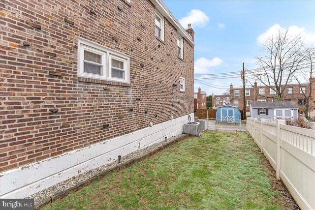 view of property exterior featuring fence, a yard, a shed, central AC, and brick siding