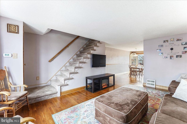 living room featuring a textured ceiling, stairway, baseboards, and wood finished floors