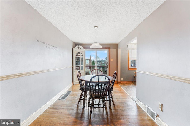 dining area featuring a textured ceiling, wood finished floors, and visible vents