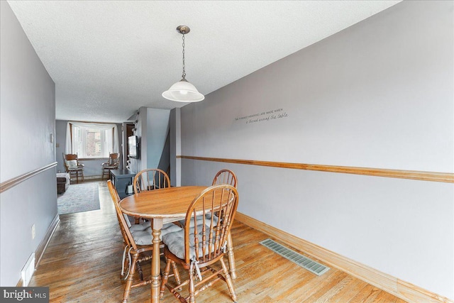 dining area featuring baseboards, a textured ceiling, visible vents, and wood finished floors