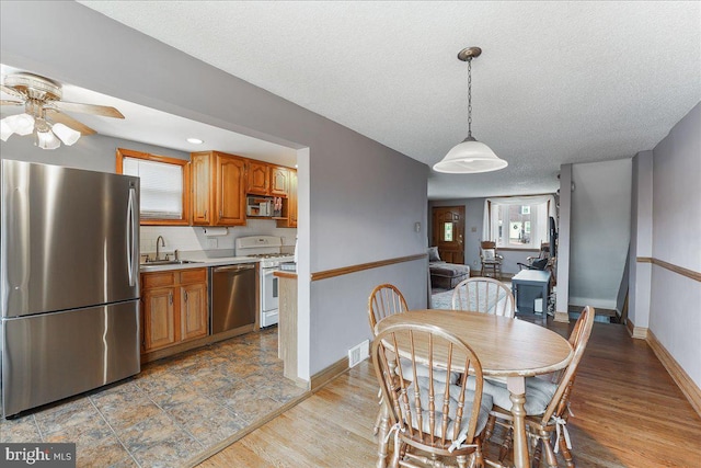 dining room featuring a textured ceiling, a ceiling fan, visible vents, baseboards, and light wood-type flooring