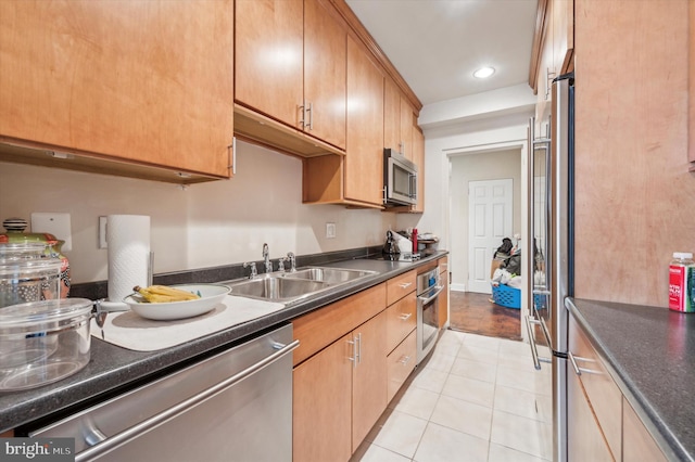 kitchen featuring light tile patterned floors, dark countertops, stainless steel appliances, a sink, and recessed lighting