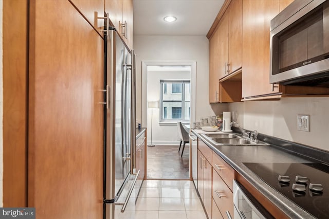 kitchen featuring light tile patterned floors, baseboards, dark countertops, stainless steel appliances, and a sink