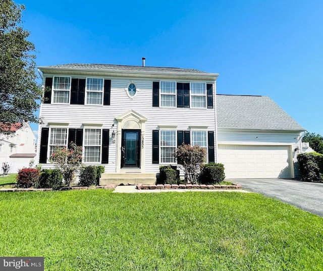 colonial-style house featuring driveway, an attached garage, and a front lawn