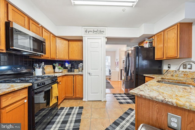 kitchen with tasteful backsplash, light tile patterned floors, light stone counters, black appliances, and a sink