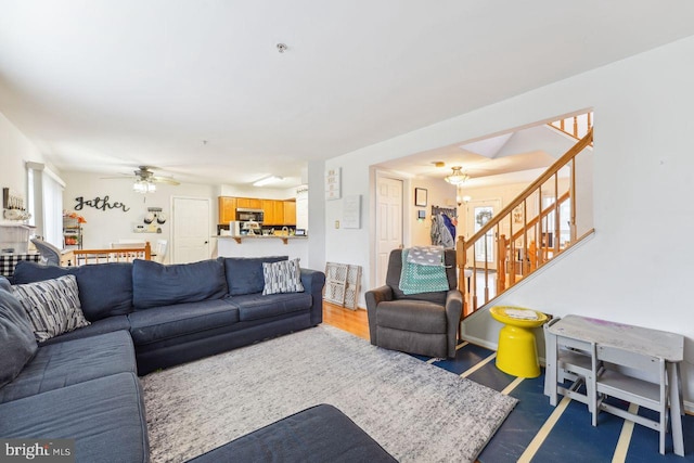 living room featuring stairway and ceiling fan with notable chandelier