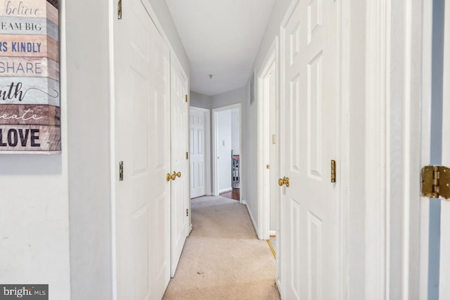 hallway featuring light colored carpet and baseboards