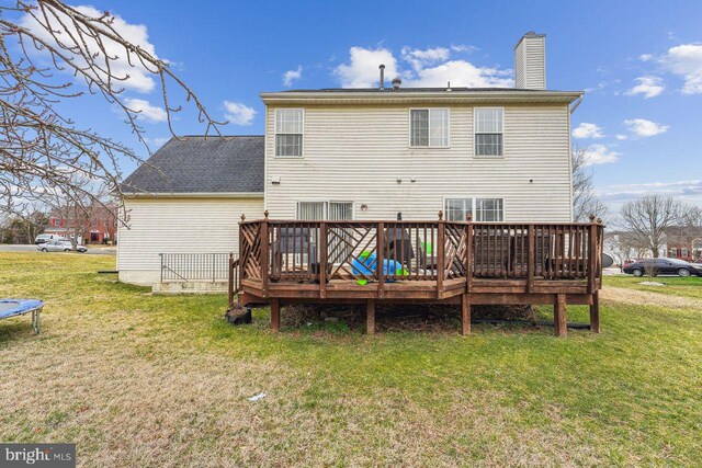 back of house featuring a yard, a trampoline, a wooden deck, and a chimney