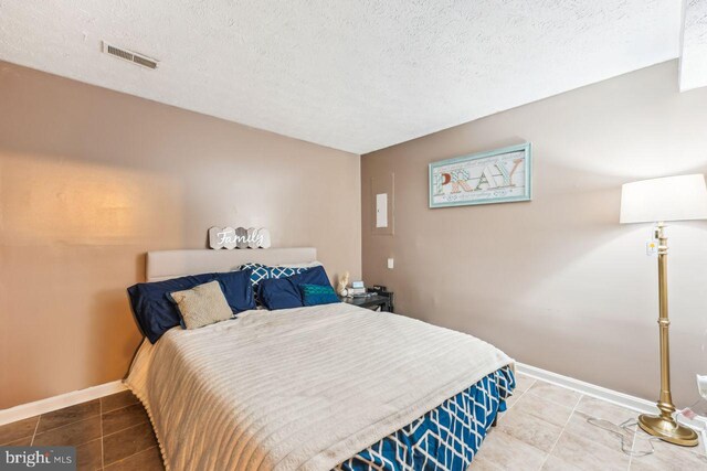 tiled bedroom with visible vents, baseboards, and a textured ceiling