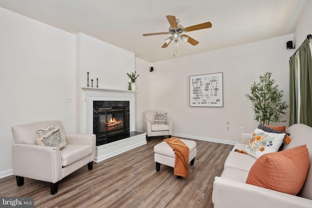 living room featuring a glass covered fireplace, baseboards, wood finished floors, and a ceiling fan