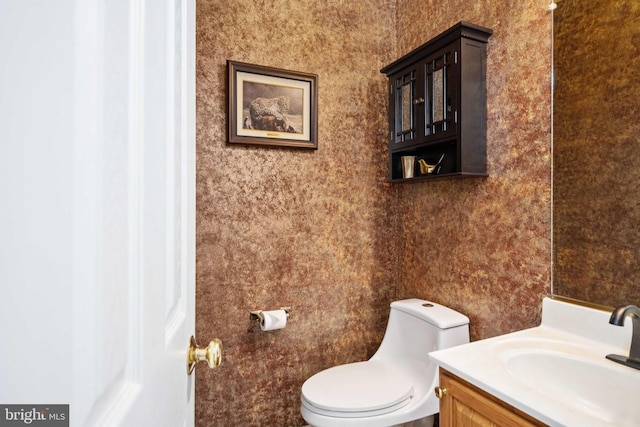 half bathroom with wallpapered walls, toilet, and vanity