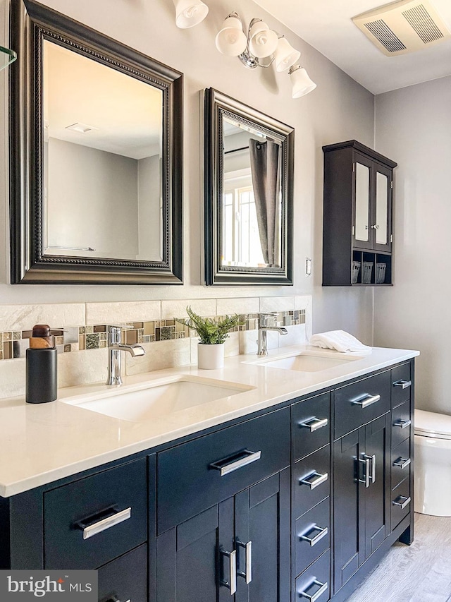 full bath with double vanity, toilet, visible vents, and a sink