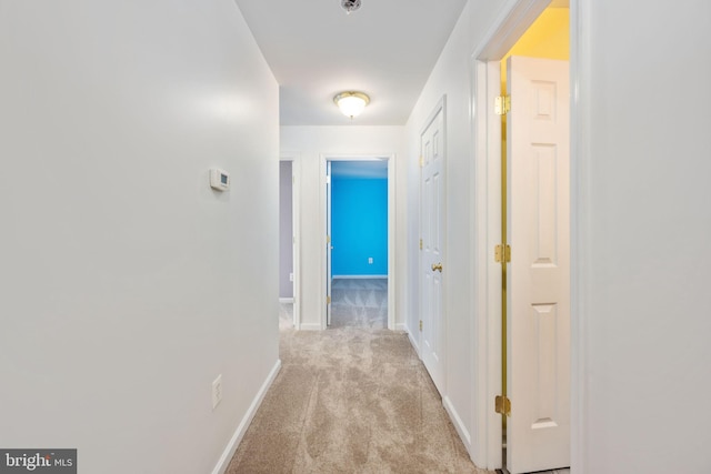 corridor featuring light colored carpet and baseboards