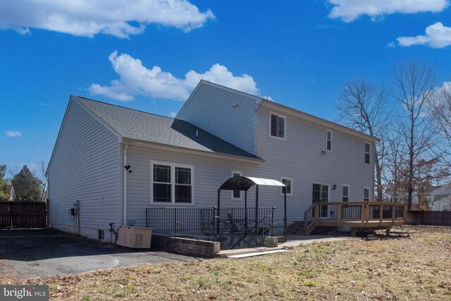 rear view of house featuring cooling unit, a shingled roof, a wooden deck, and fence