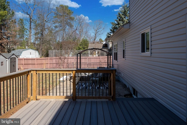 wooden terrace featuring fence, an outdoor structure, and a shed