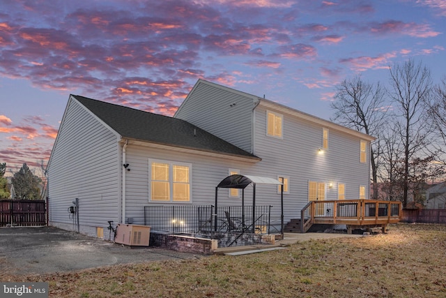 back of property at dusk featuring cooling unit, a wooden deck, a patio, and fence