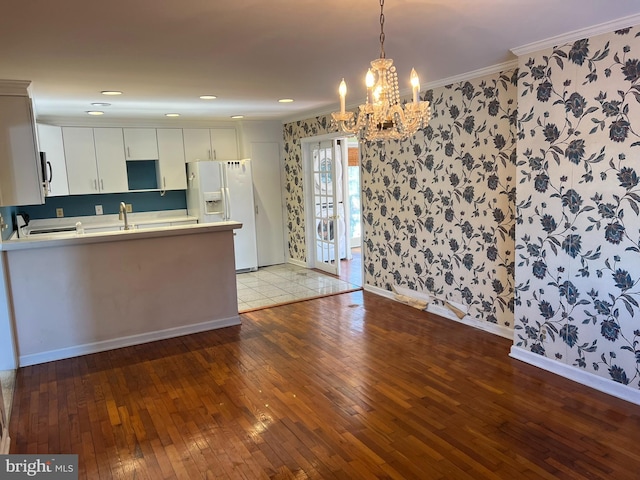 kitchen with a peninsula, white refrigerator with ice dispenser, light countertops, hardwood / wood-style floors, and crown molding