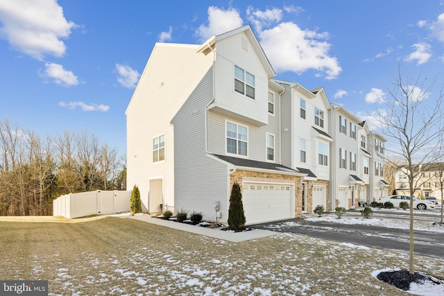 view of snowy exterior featuring a residential view, stone siding, an attached garage, and fence