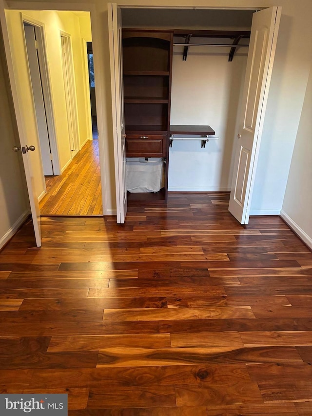 unfurnished bedroom featuring a closet, dark wood finished floors, and baseboards