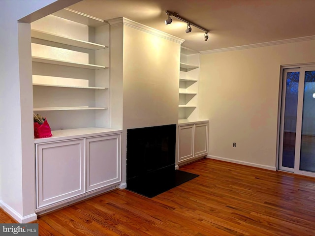 interior space with built in shelves, a fireplace with flush hearth, wood finished floors, baseboards, and crown molding