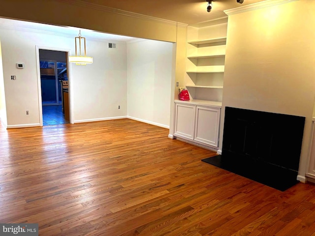 unfurnished living room featuring ornamental molding, visible vents, built in shelves, and wood finished floors