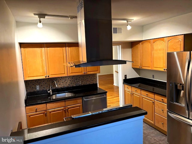 kitchen with island range hood, decorative backsplash, dark countertops, appliances with stainless steel finishes, and a sink