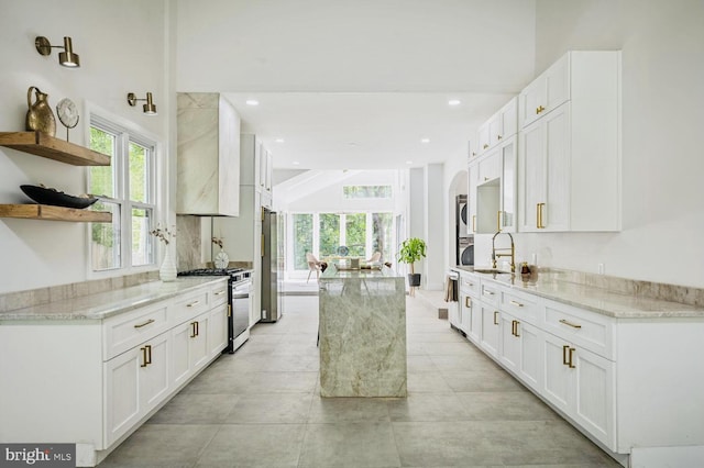 kitchen featuring light stone counters, open shelves, freestanding refrigerator, white cabinetry, and gas range