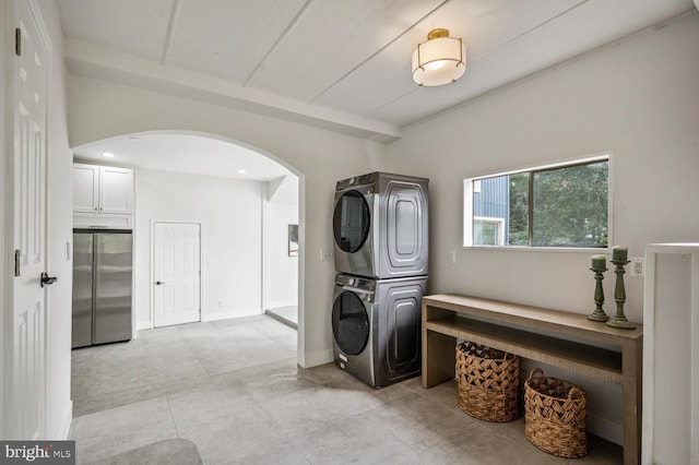 clothes washing area featuring laundry area, baseboards, arched walkways, and stacked washer / dryer